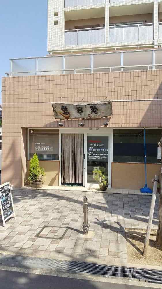 〇〇整骨院の外観。木の看板と入口ののれん、植木が目印です